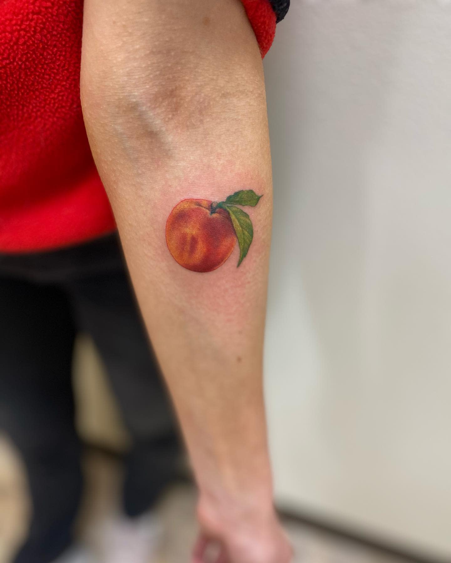 Forearm tattoo of a realistic peach with two vibrant green leaves